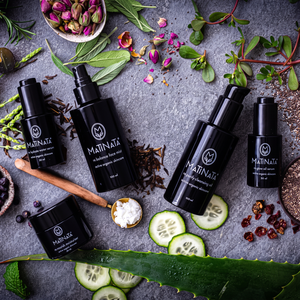 The Complete Facial Ritual by Matinata: five certified organic formulas in black glass on grey stone with cucumber, aloe and dried flowers