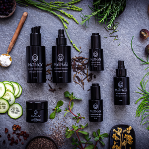 The Complete Matinata Ritual: all six certified organic Matinata formulas in black glass, flat-lay on grey stone with aloe, cucumber and herbs